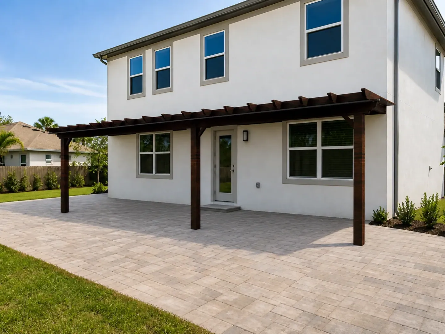 Visualisierung einer dunklen Holzpergola über der gepflasterten Terrasse eines weißen Hauses.